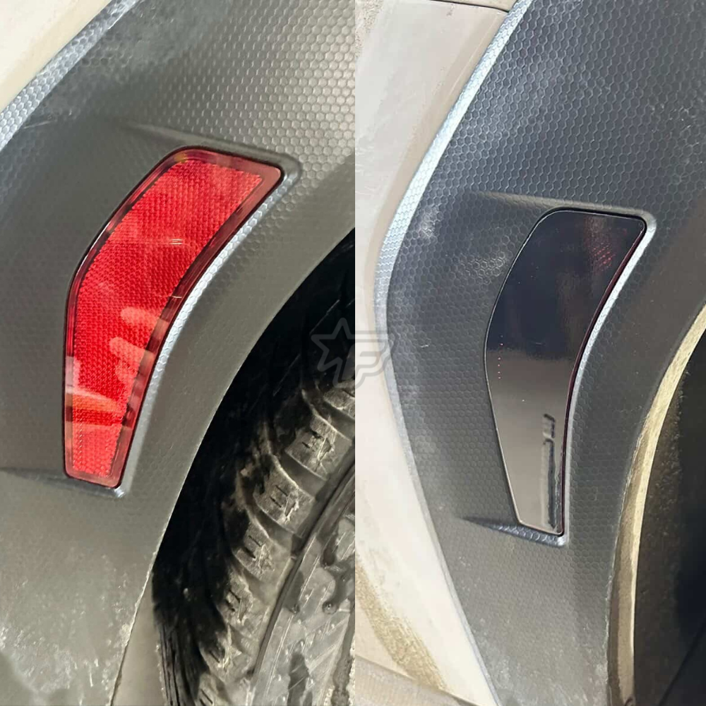 Close-up of a car's red plastic reflector and silver badge on a textured surface.