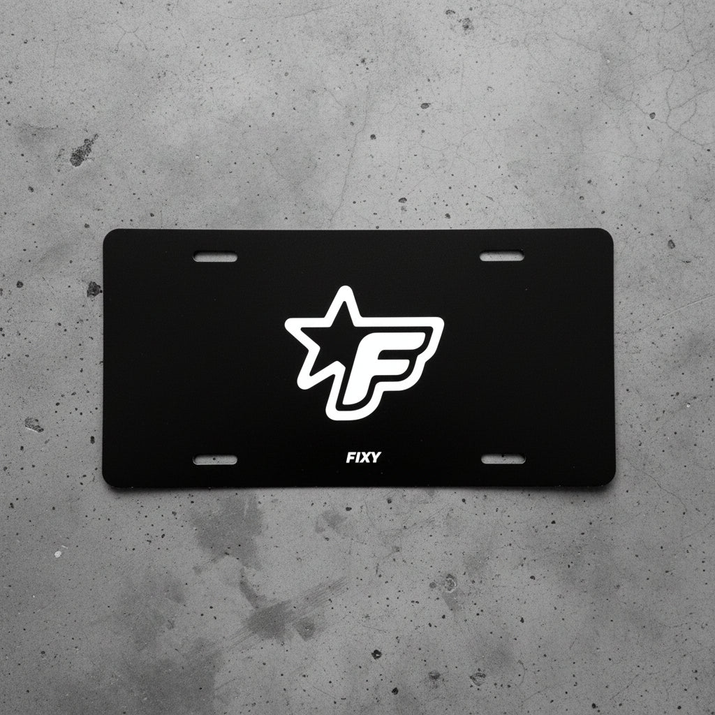 Black license plate with white logo and 'FIXY' text on a concrete surface