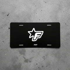 Black license plate with white logo and 'FIXY' text on a concrete surface