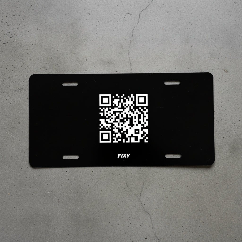 Black license plate with a QR code and 'FIXY' branding on a gray concrete surface