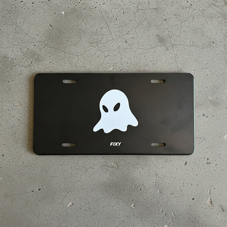 Black license plate with a white ghost design and 'FIXY' branding on a concrete background