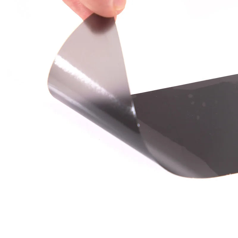 Person peeling back a sheet of black vinyl wrap on a white background