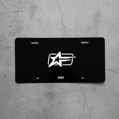 Black license plate with a white logo and 'FIXY' text on a wooden surface