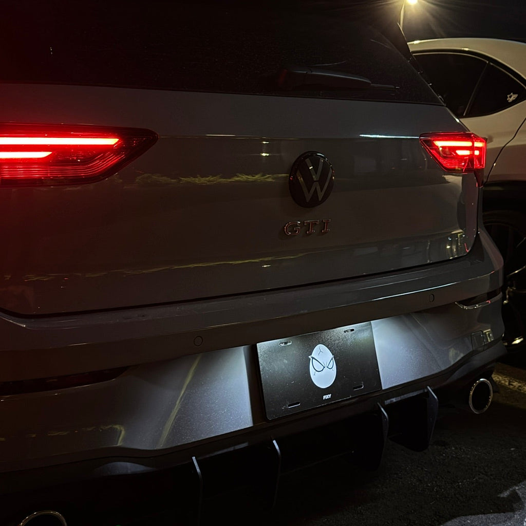 Rear view of a silver Volkswagen SUV at night with the brake lights on, showing a custom rear diffuser and license plate frame.