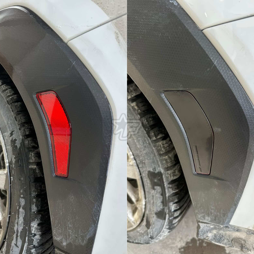 Close-up of a car's rear fender with a red reflector and black mud flap.