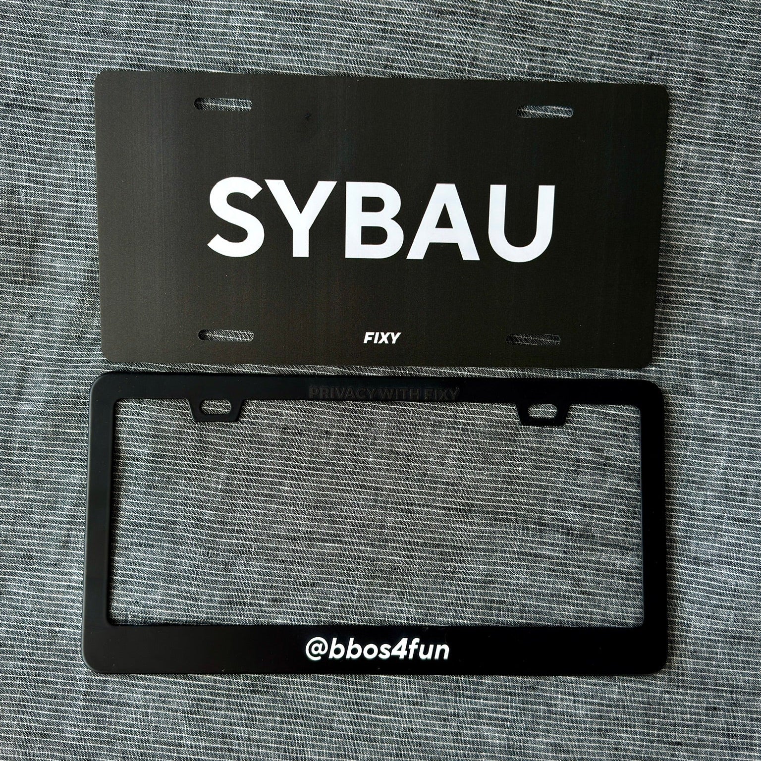 Black license plate with 'SYBAU' text on a gray textured background