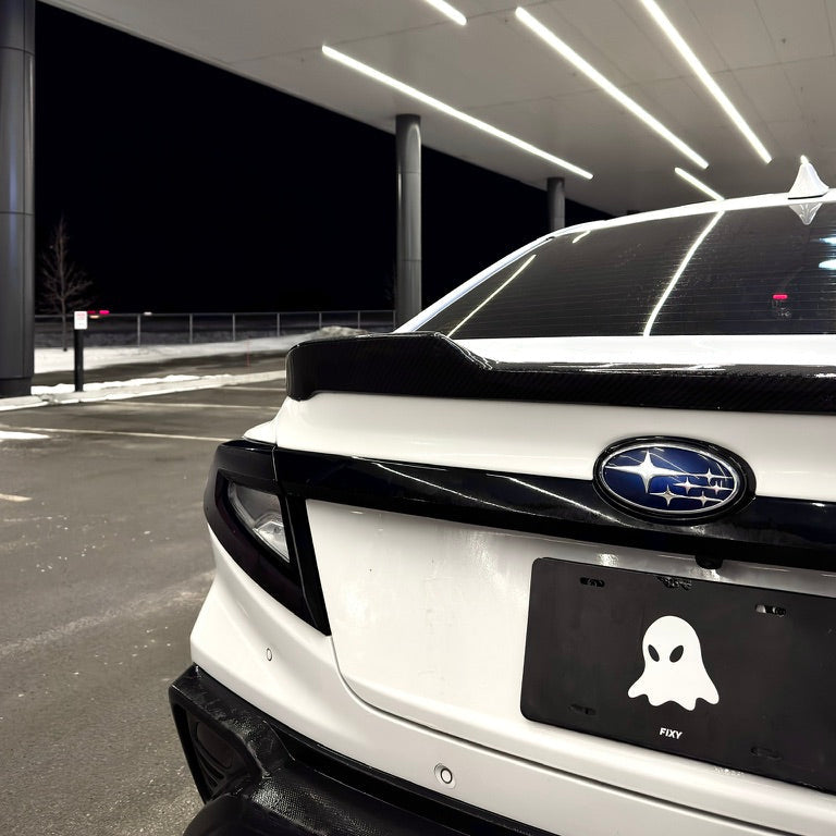 White car with a black license plate featuring a ghost icon in a dark parking garage.