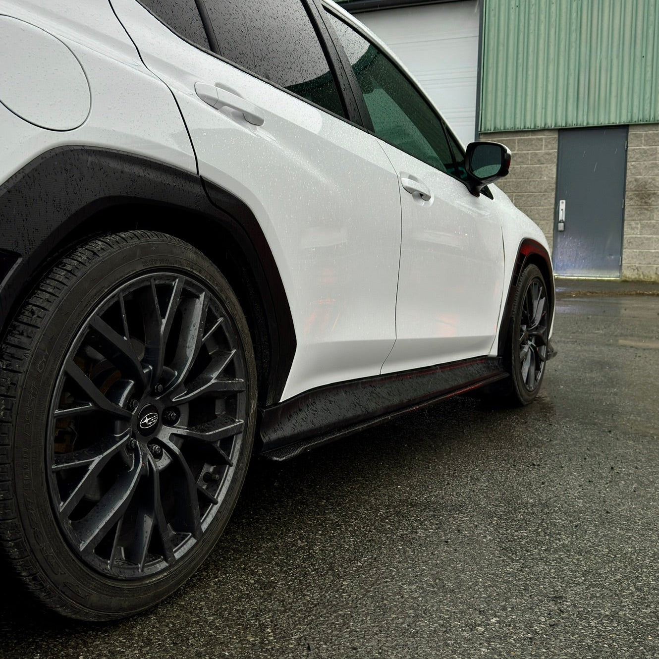 White car parked on a road with a green building in the background