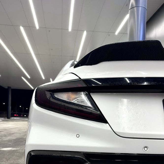 Close-up of a white car's front bumper and exhaust system in an indoor setting.