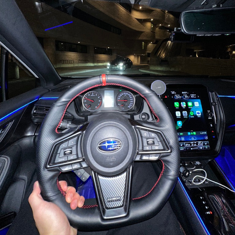 Steering wheel and dashboard of a car with a visible Subaru logo.