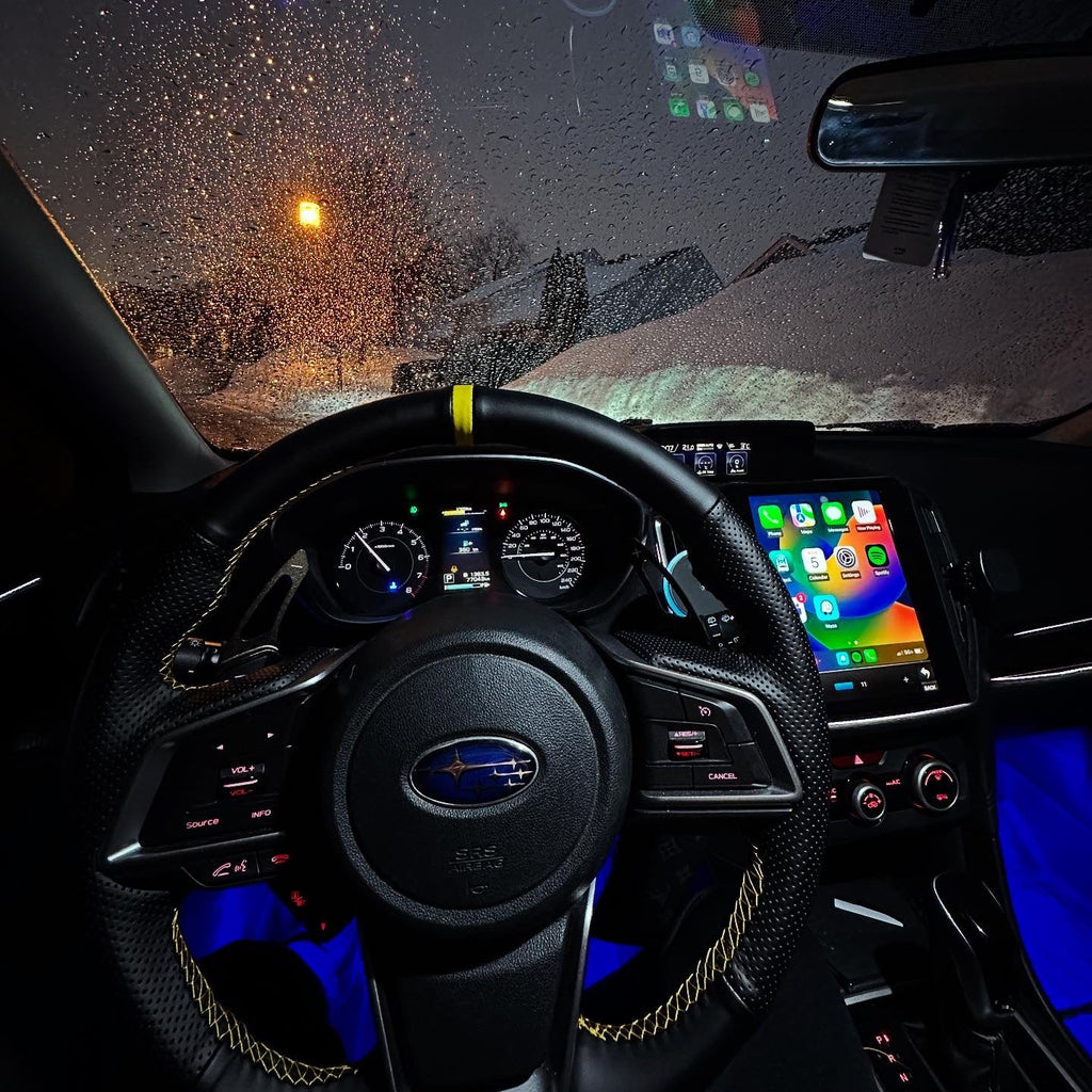 Car interior with dashboard and steering wheel during a snowy night.