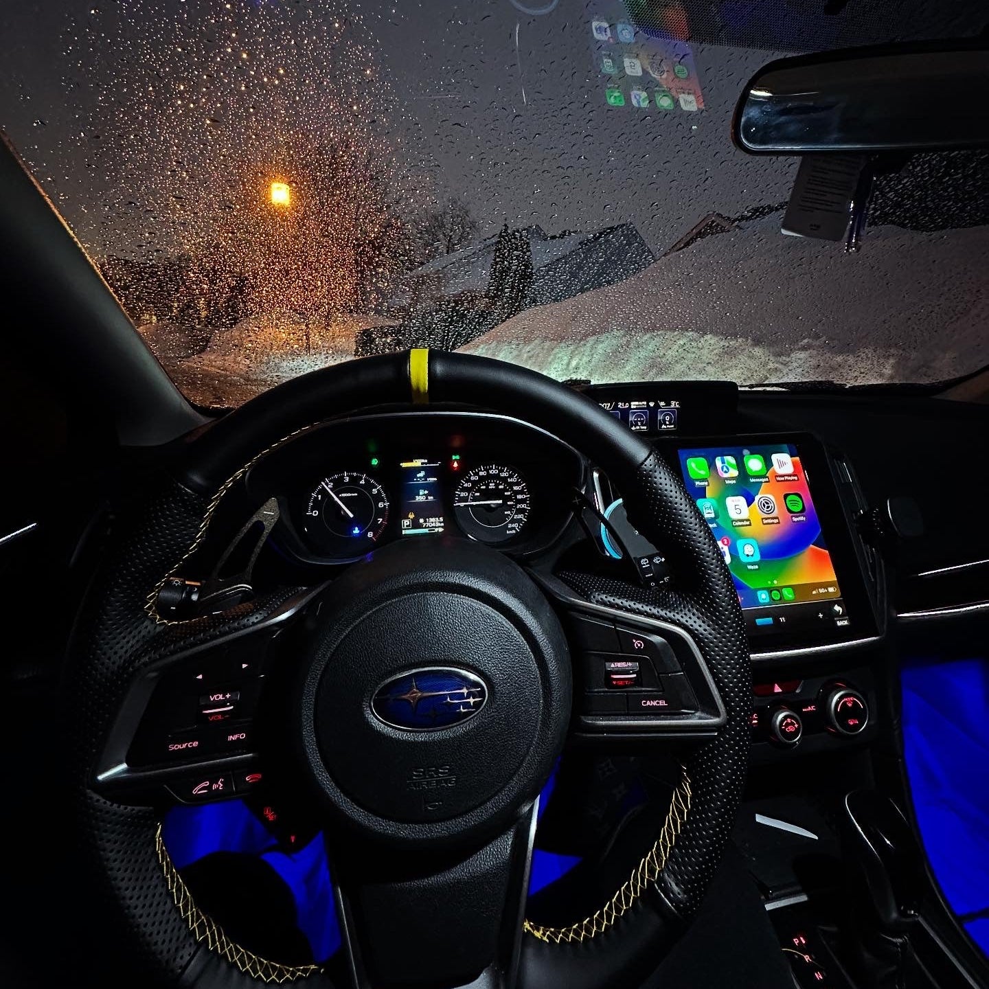 Car interior with dashboard and steering wheel during a snowy night.