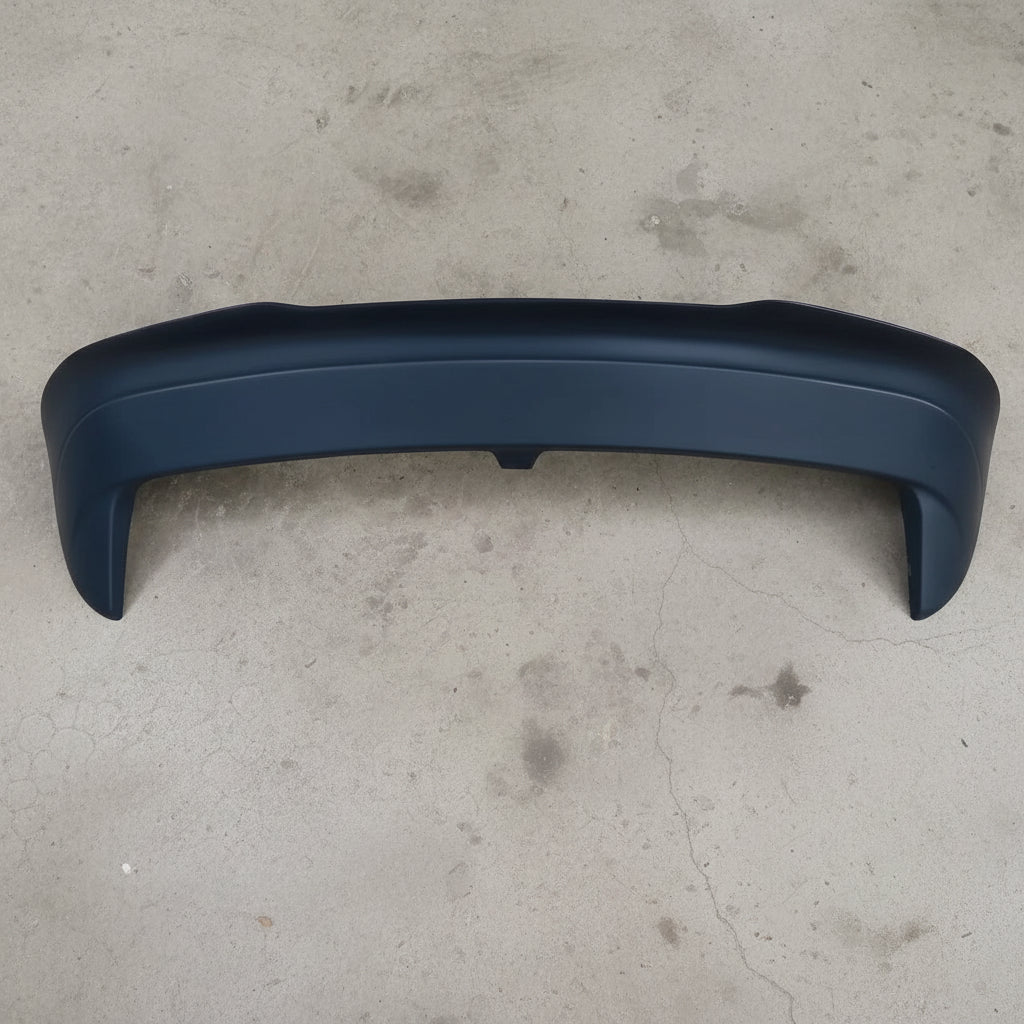 A matte black automotive rear spoiler lip mounted on a textured gray carpet background.