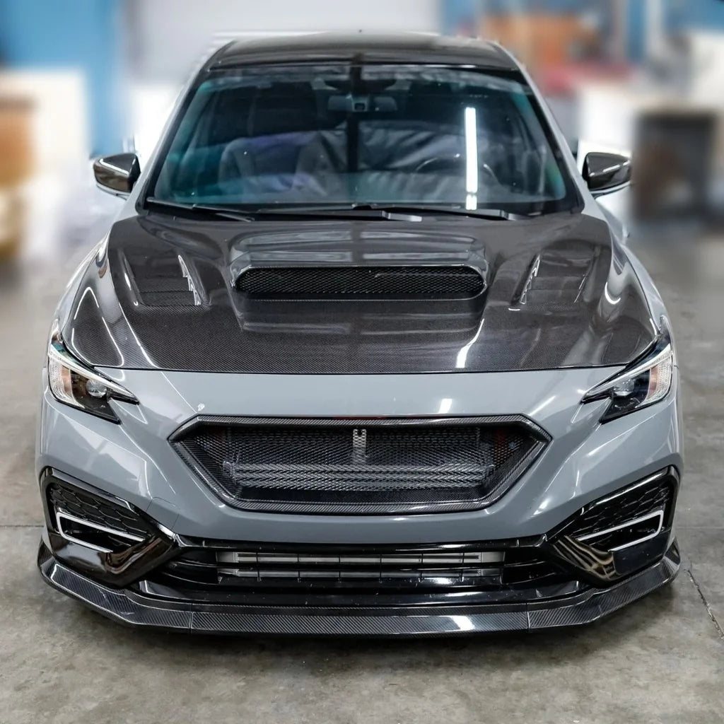 Front view of a gray car with a carbon fiber hood in a garage setting