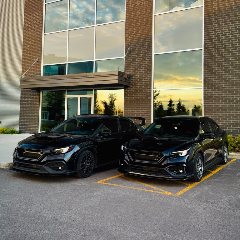 Two black cars parked side by side in front of a modern brick building with large reflective windows.