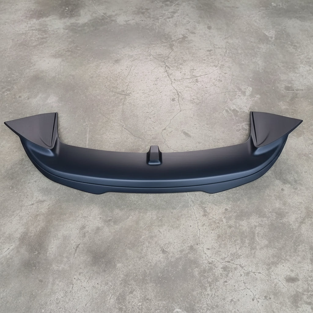 A black plastic rear trunk spoiler lip, shown from a top-down view on a textured beige carpet.