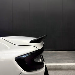 Car spoiler on a white car with a black wall in the background