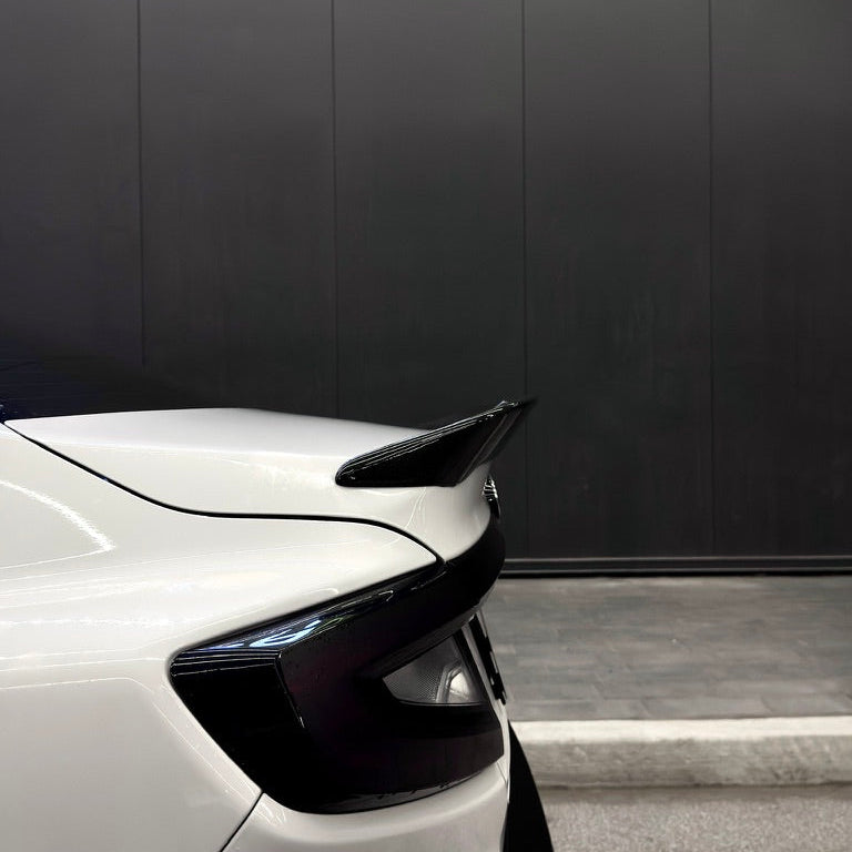 Car spoiler on a white car with a black wall in the background