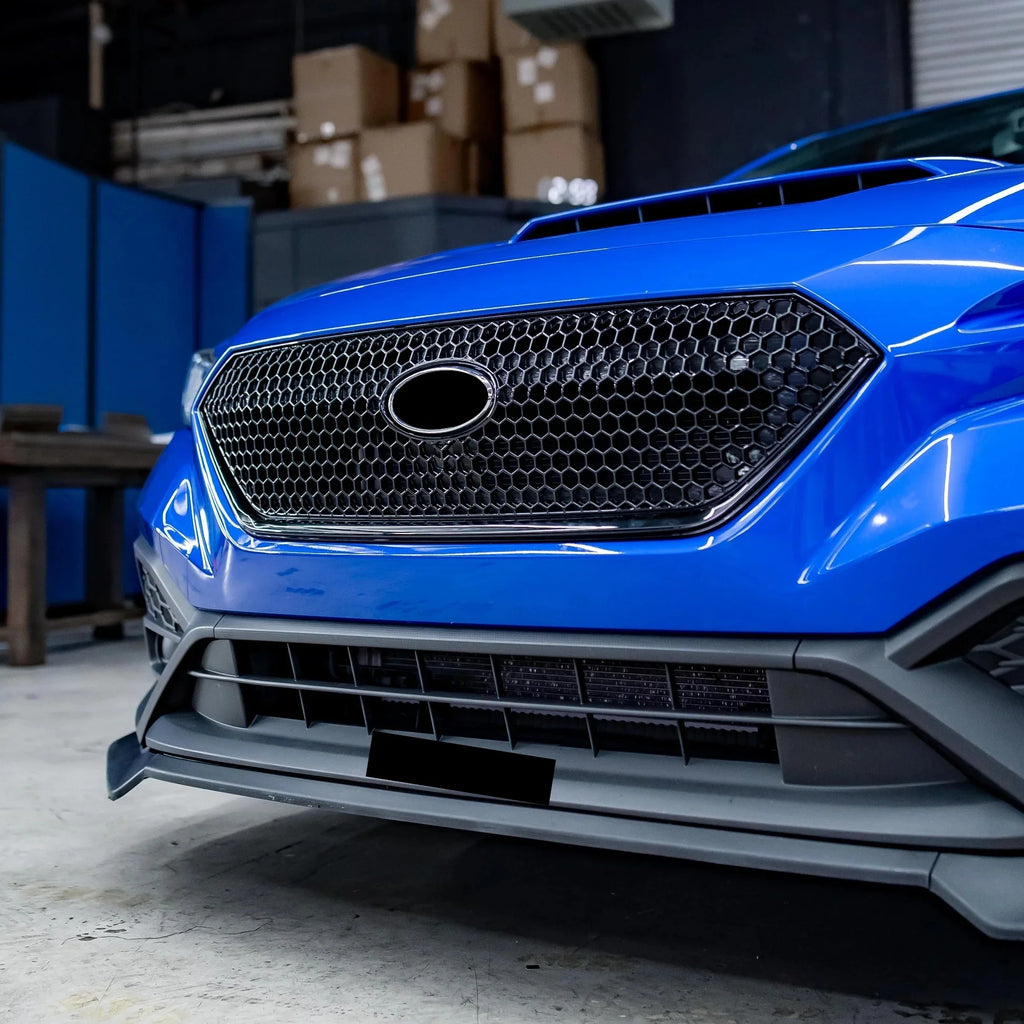 Close-up of a blue car's front grille in an indoor setting with boxes and furniture.