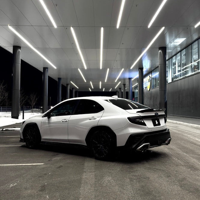 White car parked inside a modern building with a high ceiling and linear lights.