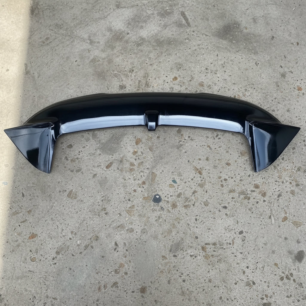 A glossy black car rear spoiler wing resting on a brown textured carpet.